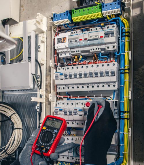 Man, an electrical technician working in a switchboard with fuses. Installation and connection of electrical equipment. Professional uses a tablet.